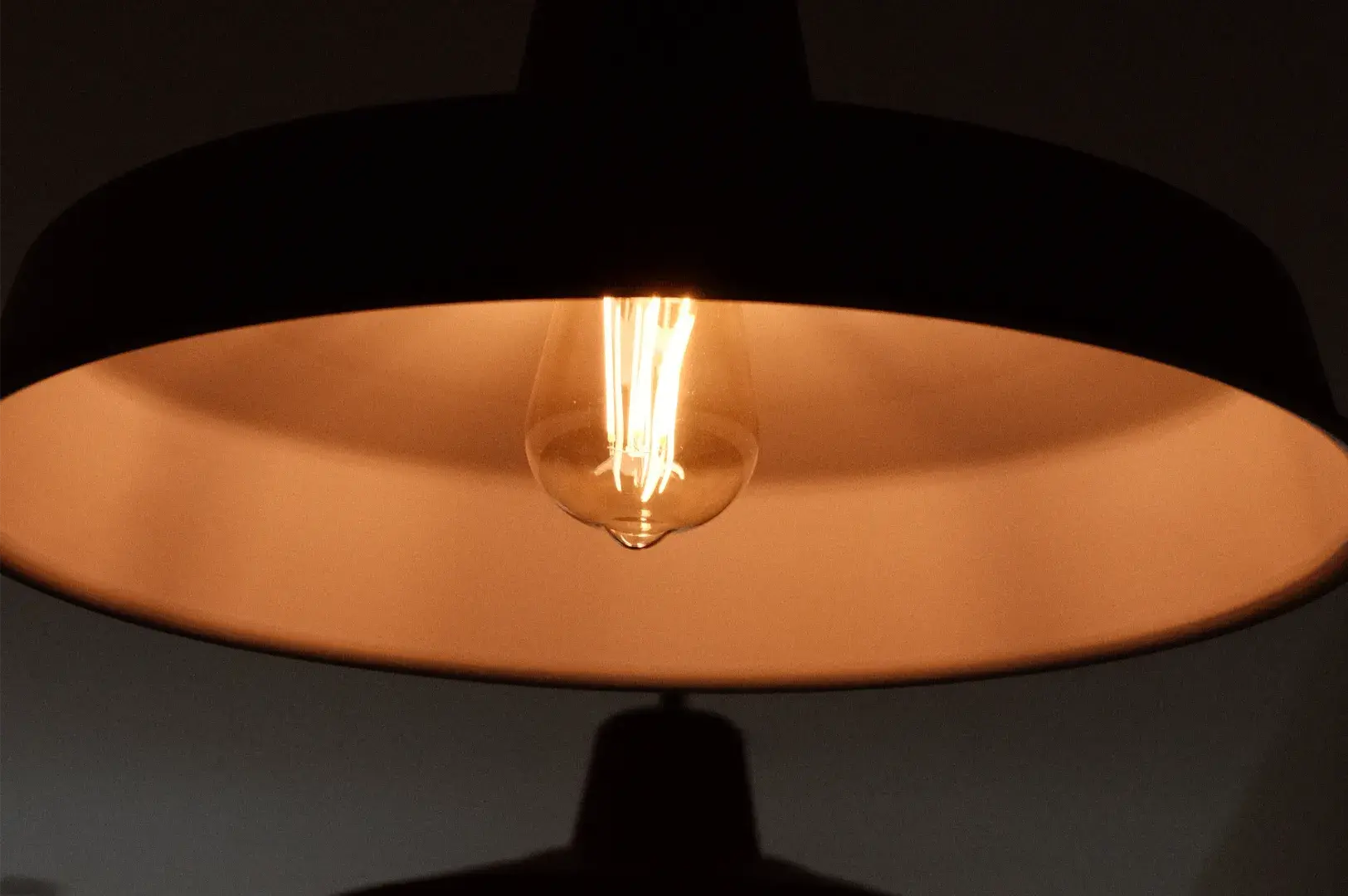 A glowing filament bulb casts a warm amber light across a wide, shallow dome-shaped fixture, creating a calm, cozy atmosphere against a dark background.