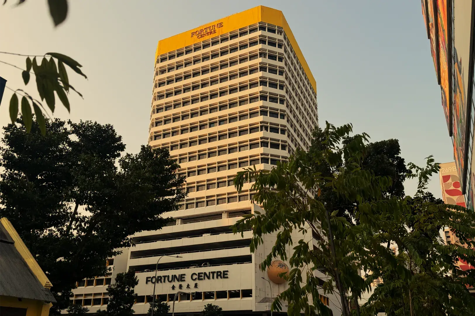 A golden high-rise labeled Fortune Centre rises above leafy trees in warm evening light, creating a calm urban cityscape.